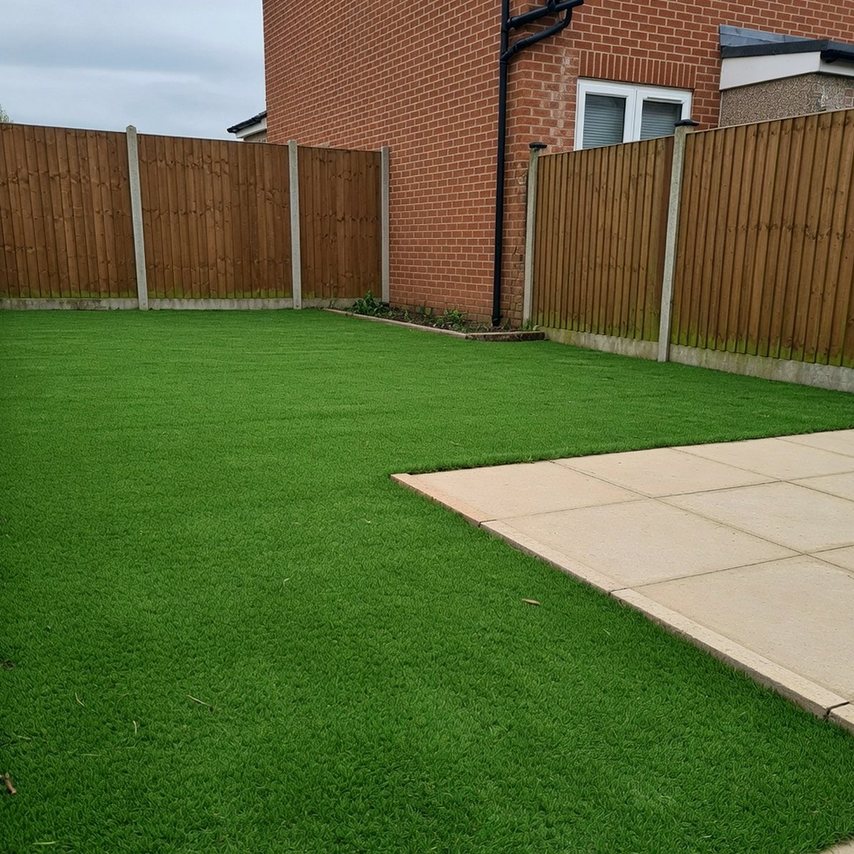 Artificial grass lawn in a British back garden next to patio slabs